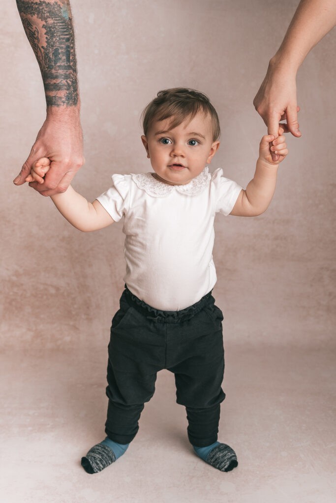 Das kleine Mädchen an der Hand von Mama und Papa während wir natürliche Familienbilder durch eine Familienfotografin gemacht haben